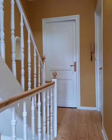 Peinture murale couleur ocre et balustres blancs dans un escalier avec parquet en bois.