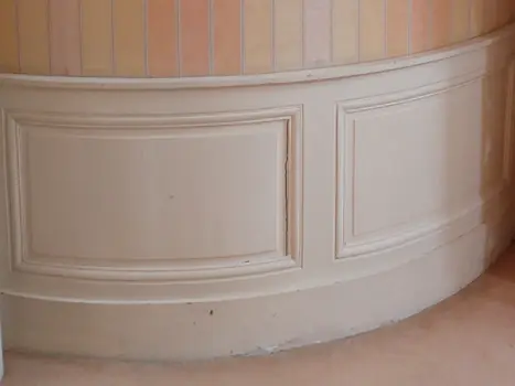 Boiserie peinte crème sur mur courbe avec papier peint rayé pastel et moulure de séparation.