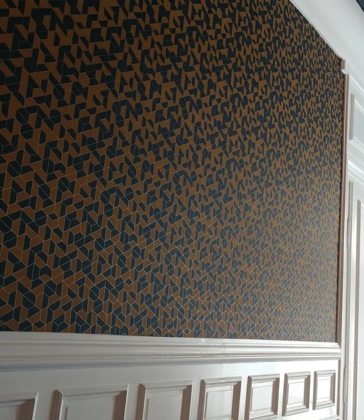 Mur revêtu de papier peint géométrique bleu et marron au-dessus de boiseries blanches peintes.