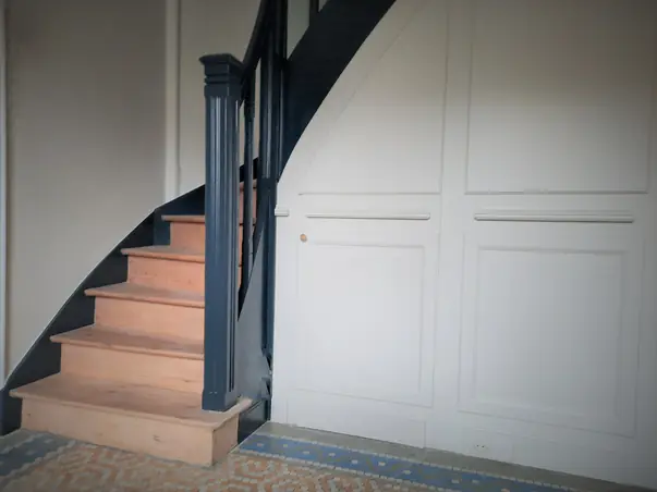 Finition peinture blanche sur boiserie murale et escalier en bois avec garde-corps sombre.