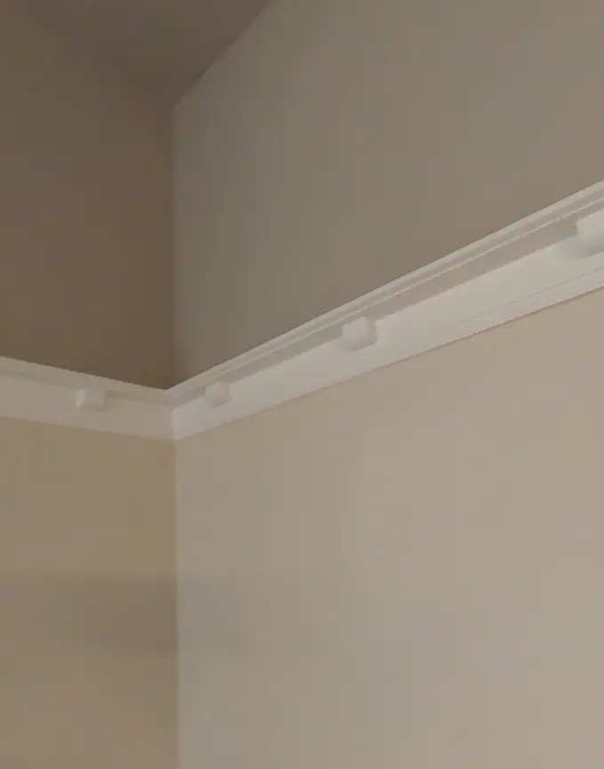 Pose de moulure blanche à l'angle du plafond sur murs peints beige.