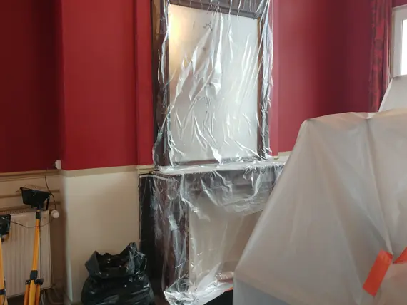 Protection systématique des meubles et miroirs par film plastique sur chantier peinture murale rouge.