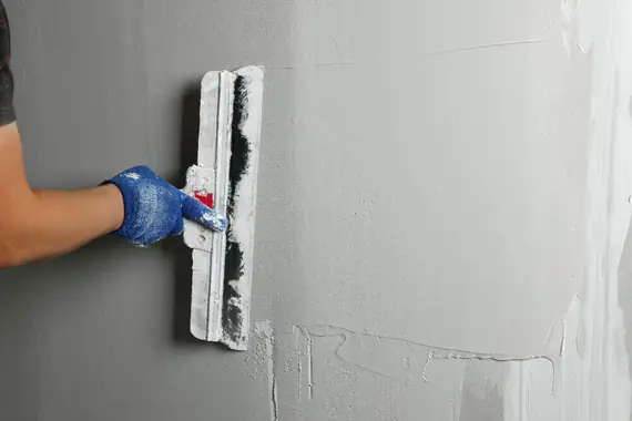 Application d'enduit pelliculaire gris sur mur avec truelle pour préparation de support