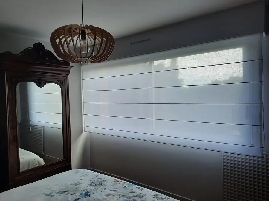 Store enrouleur blanc translucide sur fenêtre de chambre, mur peint gris clair finition velours.